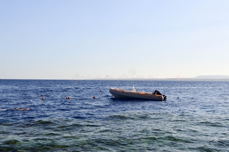 Bateau gris gonflable, un canot automobile avec un moteur sur une mer bleue de sel contre le contexte des montagnes éloignées images libres de droits Bateau gris gonflable, un canot automobile avec un moteur sur une mer bleue de sel contre le contexte des montagnes éloignées images libres de droits