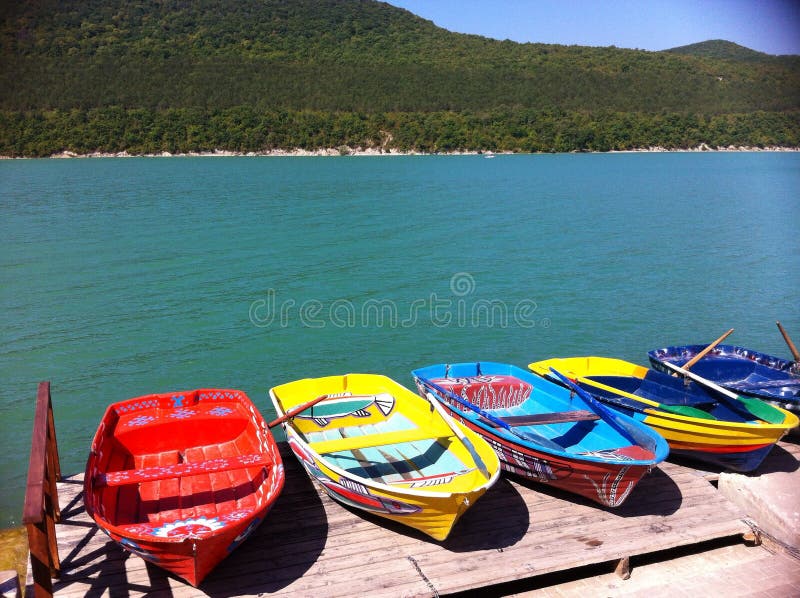 Colorful (yellow and red) boats on beautiful lake. Beautiful turquoise lake with mountains in background. Several boats moored to the shore. Colorful (yellow and red) boats on beautiful lake. Beautiful turquoise lake with mountains in background. Several boats moored to the shore.