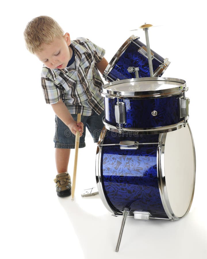 An adorable preschooler bending over a drum set to beat the base drum with a drumstick. On a white background. An adorable preschooler bending over a drum set to beat the base drum with a drumstick. On a white background.