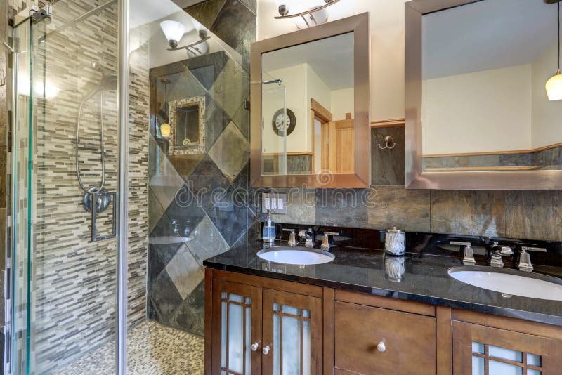 Bathroom interior with grey tiles and wak in shower with dark wood classic vanity with black countertop and two mirrors