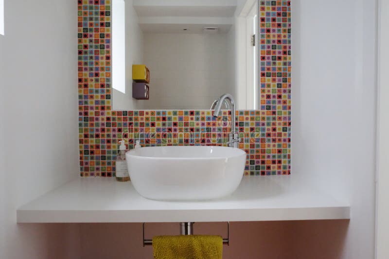 Bathroom wash basin with colorful glass mosaic tiles and mirror inset into the tiles