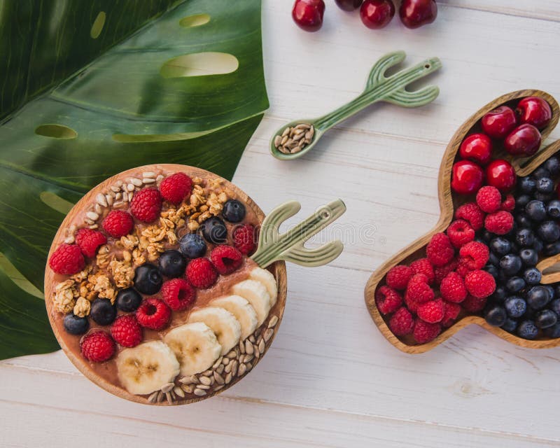 Batido de Acai, granola, sementes, frutos frescos em uma bacia de madeira com colher do cacto Placa enchida com as bagas no branc imagens de stock Batido de Acai, granola, sementes, frutos frescos em uma bacia de madeira com colher do cacto Placa enchida com as bagas no branc imagens de stock