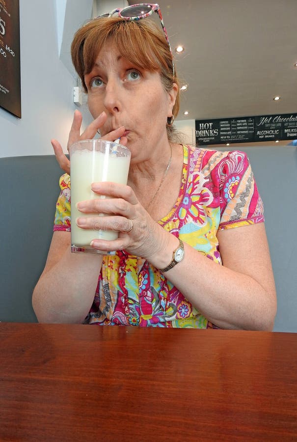 Batido de leche de consumición de la mujer en café imagen de archivo libre de regalías Batido de leche de consumición de la mujer en café imagen de archivo libre de regalías