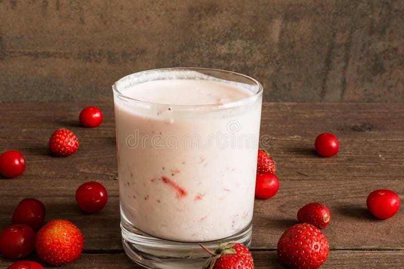 Batido do iogurte da morango e da cereja em um vidro na tabela de madeira imagem de stock Batido do iogurte da morango e da cereja em um vidro na tabela de madeira imagem de stock