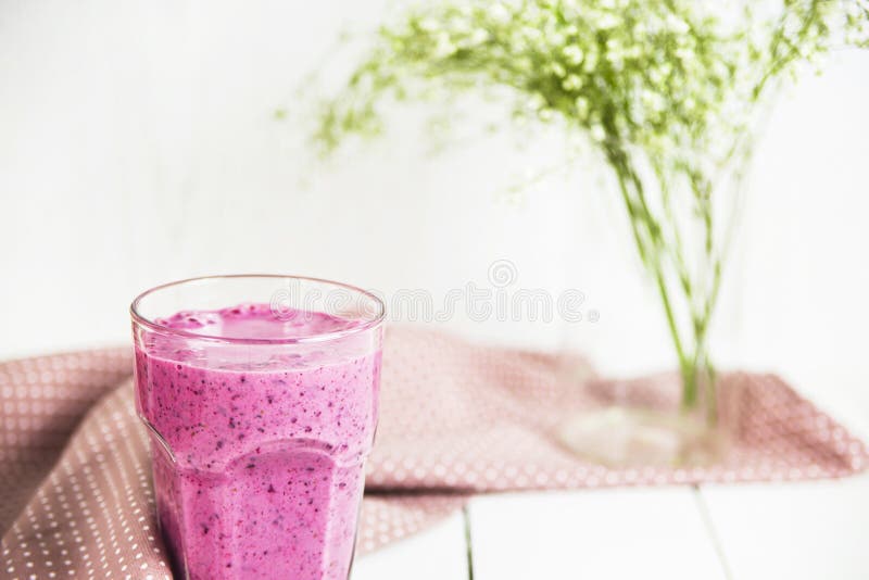 Batidos do corinto em uma tabela branca. Batidos do corinto da banana em um vidro em uma tabela branca ao lado de um guardanapo cor-de-rosa nos salpicos Na perspectiva das cores brancas e verdes delicadas