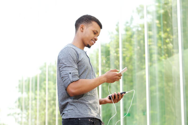 Batteri och mobiltelefon för ung afrikansk amerikanman hållande yttre royaltyfria foton Batteri och mobiltelefon för ung afrikansk amerikanman hållande yttre royaltyfria foton