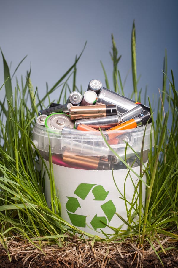Battery Recycle Bin with Old Element on Wood Table in Grass Stock Photo