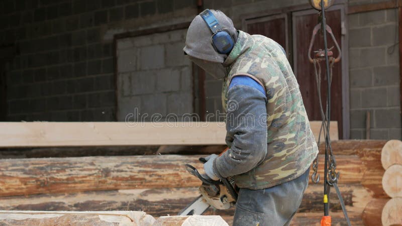 Bauarbeiter schneidet hölzerne Kettensäge für zukünftiges Haus Schutzmaske und Kopfhörer auf dem Kopf des Erbauers und des a