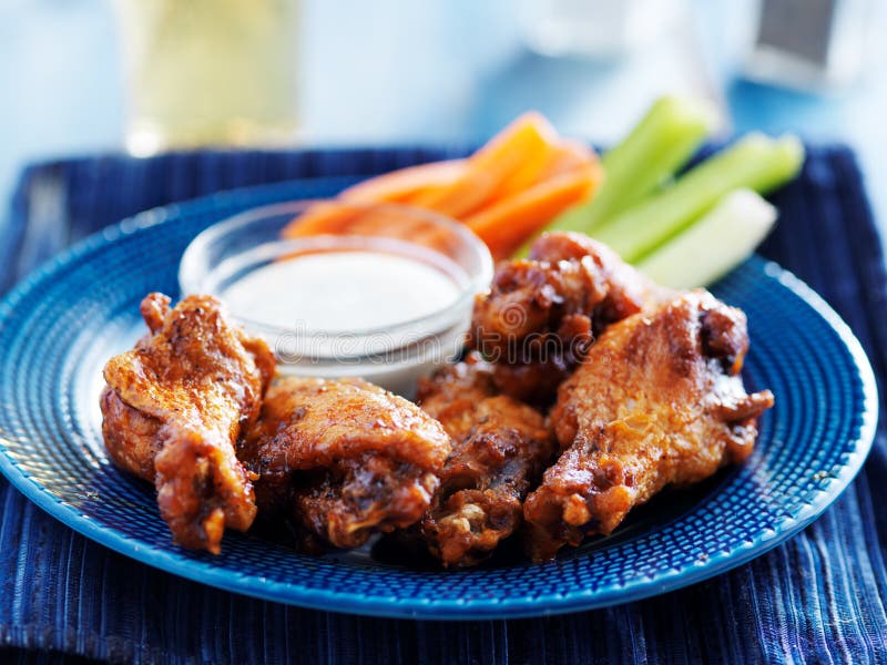 Bbq buffalo chicken wings on blue plate with ranch dip and celery sticks with selective focus. Bbq buffalo chicken wings on blue plate with ranch dip and celery sticks with selective focus