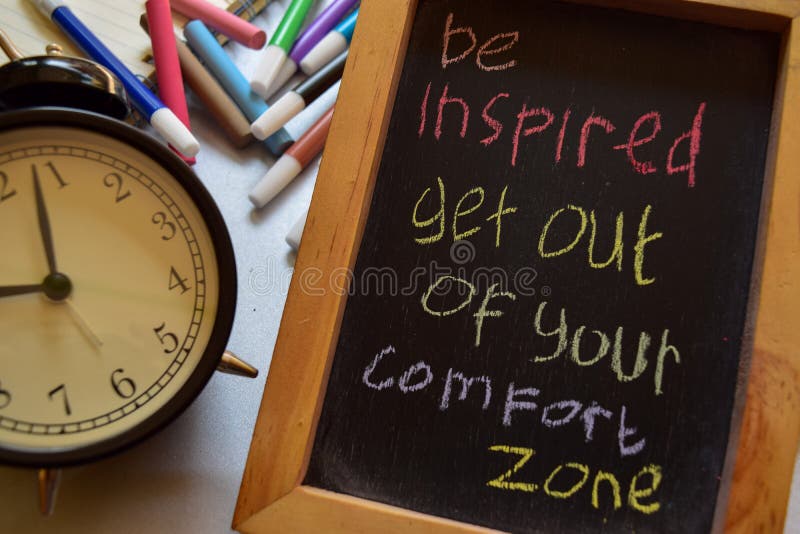 Be inspired get out of your comfort zone on phrase colorful handwritten on chalkboard, alarm clock