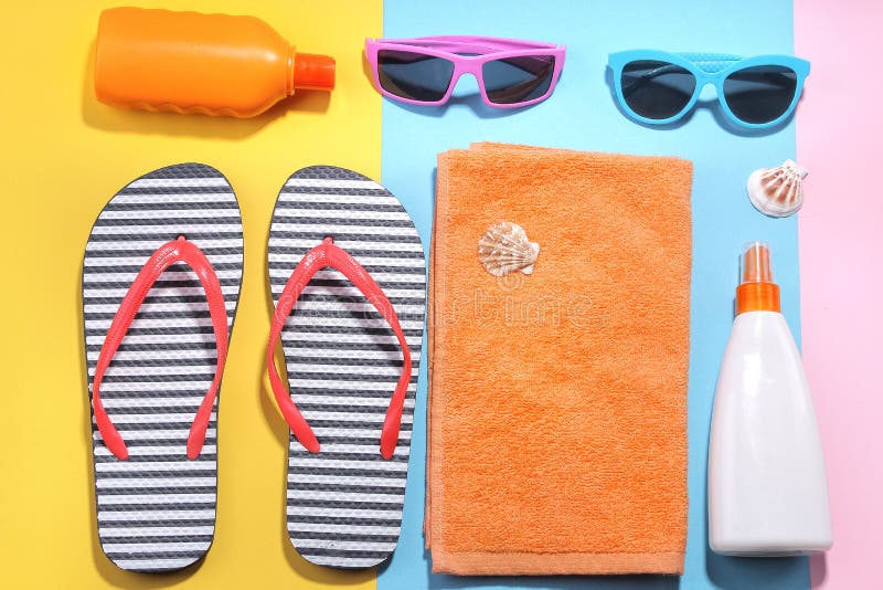 Beach accessories. Various creams, glasses, hat and towel with sea shells on a colored background. Flat Lay.