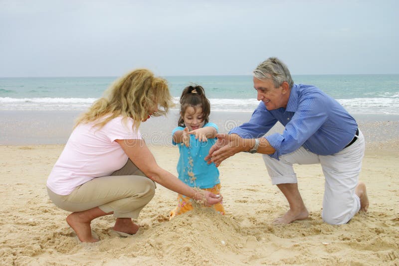 Bambina che gioca sulla spiaggia con i suoi nonni.