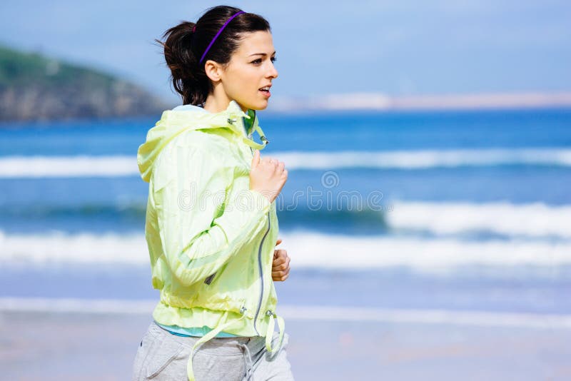 Fitness brunette woman running at Gijon beach, Asturias, Spain. Female runner training outdoor on spring sunny day. Fitness brunette woman running at Gijon beach, Asturias, Spain. Female runner training outdoor on spring sunny day.