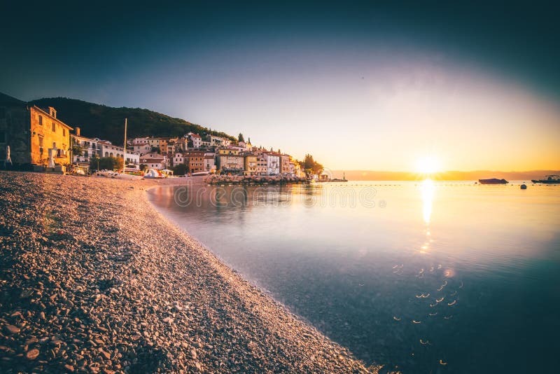 Beautiful pebbly beach in MoÅ¡Ä‡eniÄka Draga bay at sunrise, with historical town of Istria in the background, Croatia
