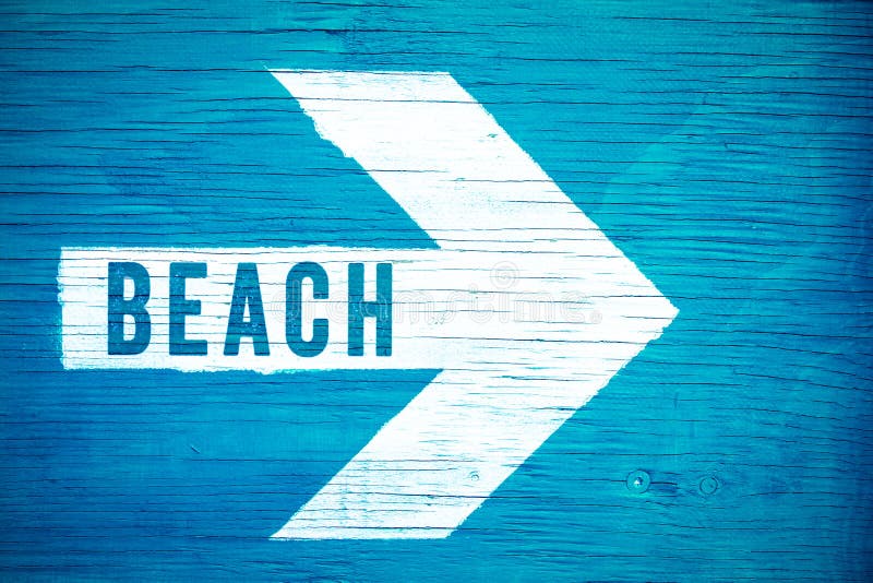 Beach text sign written on a white directional arrow pointing towards right manually painted on a blue wooden signboard stock images