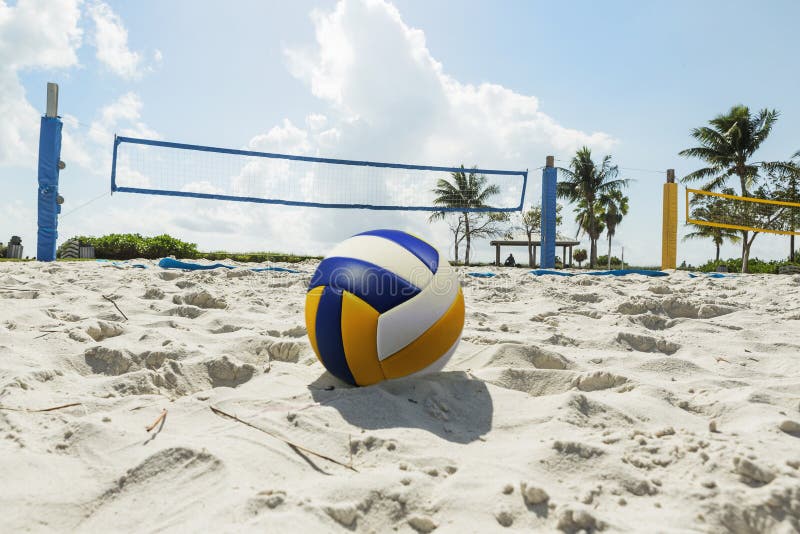 Volley ball in the foreground on the sand beach in the background volleyball net and palm trees, sunny day at the beach. Florida. Volley ball in the foreground on the sand beach in the background volleyball net and palm trees, sunny day at the beach. Florida