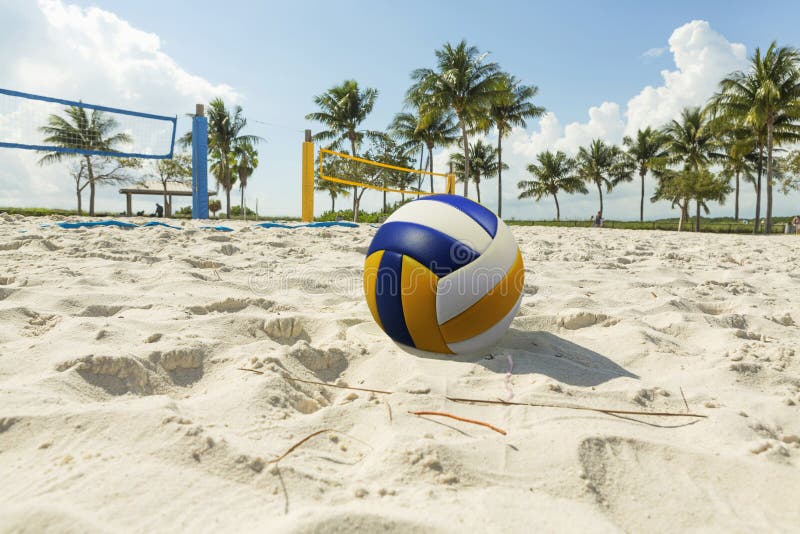 Volley ball in the foreground on the sand beach in the background volleyball net and palm trees, sunny day at the beach. Florida. Volley ball in the foreground on the sand beach in the background volleyball net and palm trees, sunny day at the beach. Florida