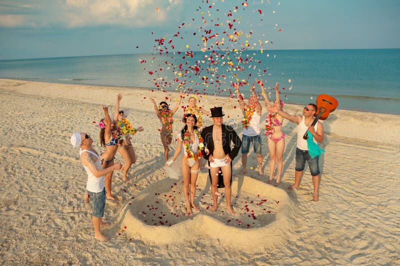 Beach wedding of happy newlywed couple around their friends