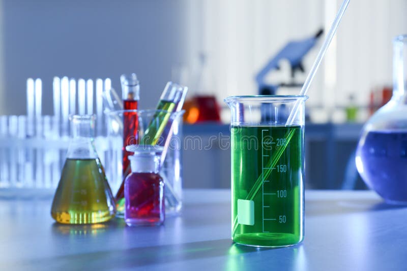 Beaker with Color Liquid on Table Against Blurred Background. Chemistry Glassware Stock Photo