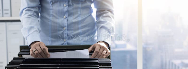 Female office worker searching files and paperwork in the archive, she is checking folders in a filing cabinet. Female office worker searching files and paperwork in the archive, she is checking folders in a filing cabinet