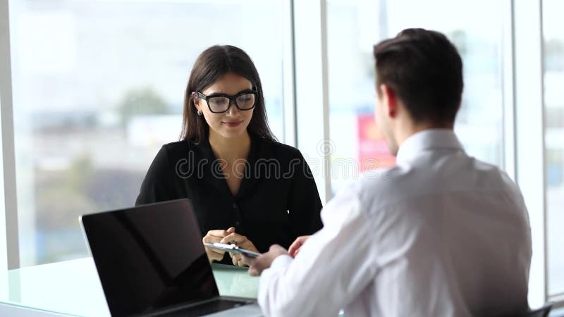 Beambtezitting bij bureau in bureau die laptop met behulp van, terwijl vrouwen die telefoon op de achtergrond spreken