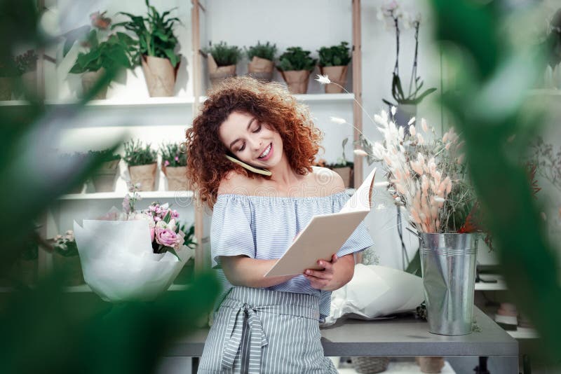 Beaming curly-haired florist filling her notebook with orders stock photography