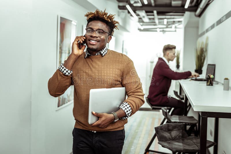 Beaming guy in clear glasses with dreadlocks having conversation on smartphone stock photo Beaming guy in clear glasses with dreadlocks having conversation on smartphone stock photo