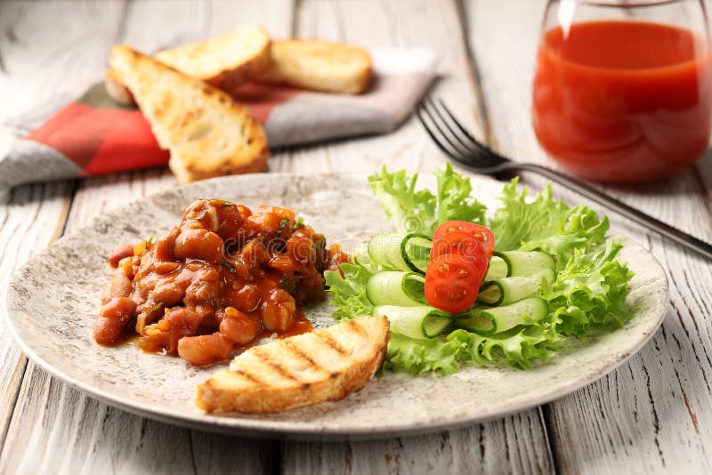 Beans in tomato sauce with garlic and cilantro, served on a white plate with lettuce, thinly sliced â€‹â€‹cucumbers, tomatoes