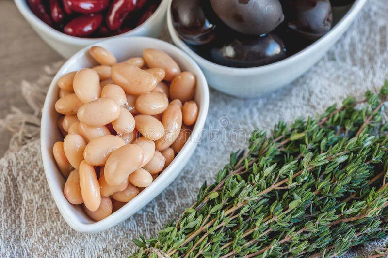 Beans are white and red with large black olives in white small cups with green leaves of arugula and Lollo Ross prepared. For salad with thyme. Prevention of royalty free stock image Beans are white and red with large black olives in white small cups with green leaves of arugula and Lollo Ross prepared. For salad with thyme. Prevention of royalty free stock image