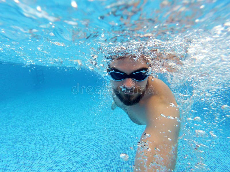 Beard man with glasses swimming under water in the pool