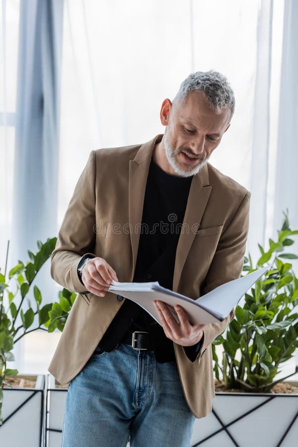 Businessman looking at document while holding folder in office. Bearded businessman looking at document while holding folder in office