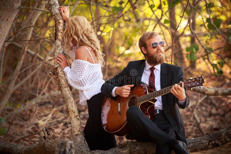 Bearded guitarist and girl sit on tree branch