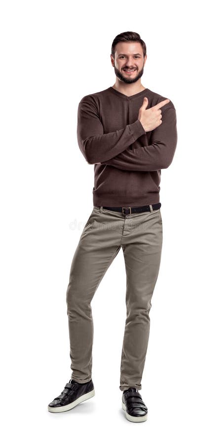 A bearded man in casual clothes keeps one leg bent white smiling and showing direction with one of crossed hands.