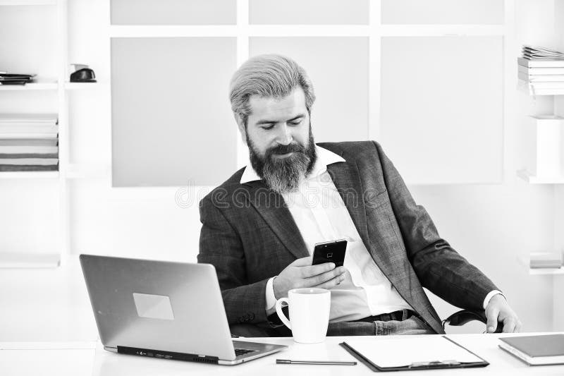 Bearded man sitting at desk in office. confident brutal businessman. Elegant businessman analyzing data in smartphone. Quarantine royalty free stock photo