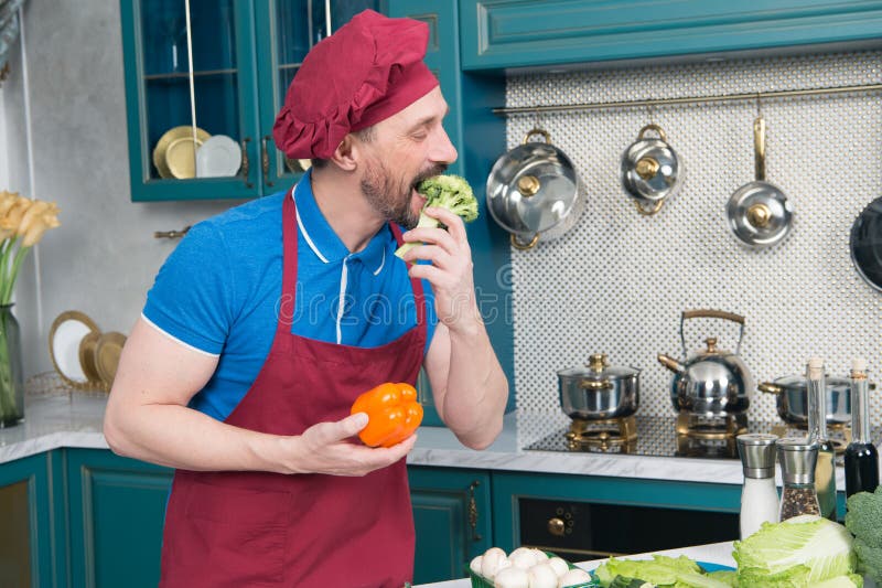 Bearded Man taste fresh broccoli and paprika before cooking at kitchen. Man loves vegetarian food concept royalty free stock photo Bearded Man taste fresh broccoli and paprika before cooking at kitchen. Man loves vegetarian food concept royalty free stock photo