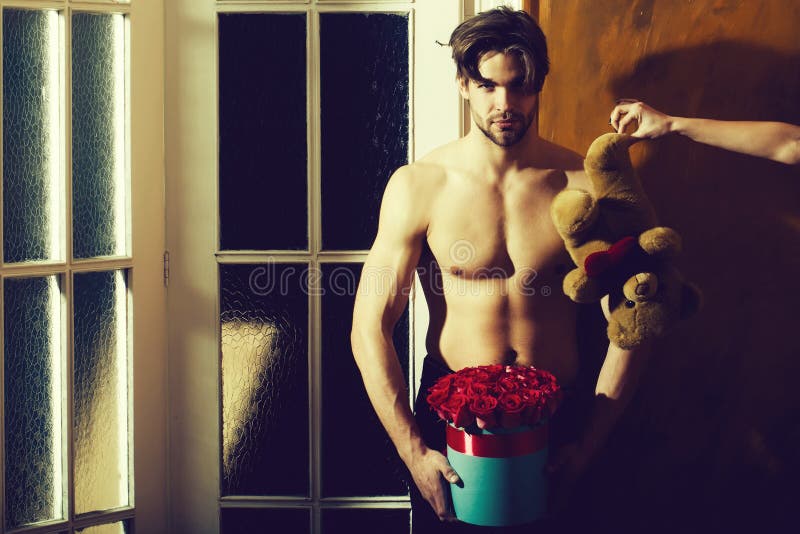 Bearded muscular man with sexy body holds red rose box