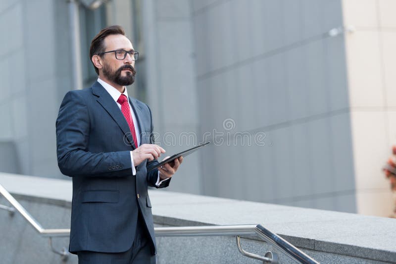 Bearded professional man broker standing outdoor while holding digital tablet in his hands. Modern businessman thinking overview royalty free stock photography Bearded professional man broker standing outdoor while holding digital tablet in his hands. Modern businessman thinking overview royalty free stock photography
