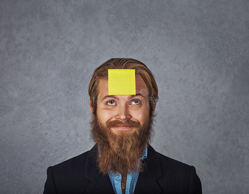 Bearded smiling business man looking up to the sticker stick on his head forehead