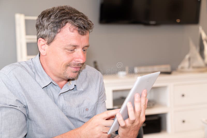 Bearded smiling man using tablet for video conversation while relaxing on sofa in modern house in Concept of business people stock photography
