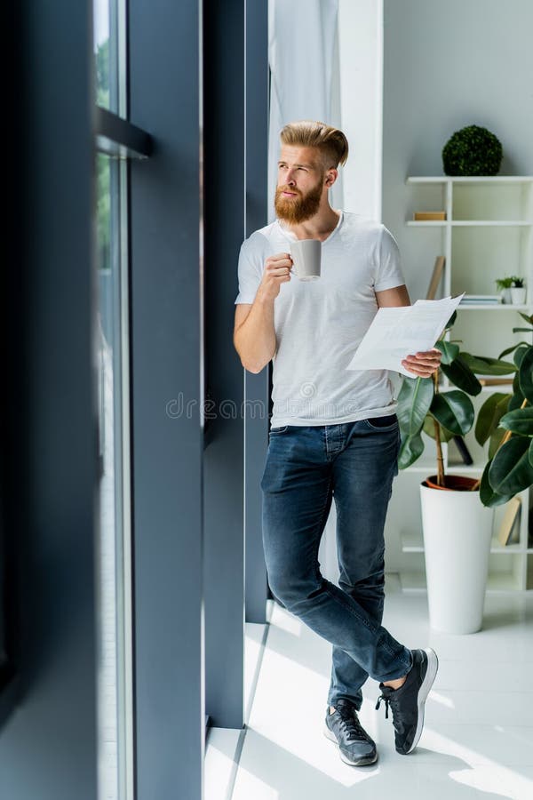 Bearded young businessman working at modern office.Man wearing white t-shirt and making notes on the documents.