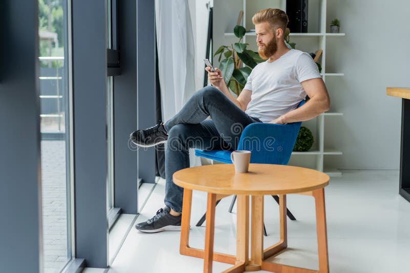 Bearded young businessman working at modern office.Man wearing white t-shirt and making notes on the documents.