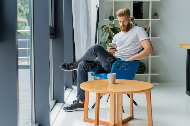 Bearded young businessman working at modern office.Man wearing white t-shirt and making notes on the documents.