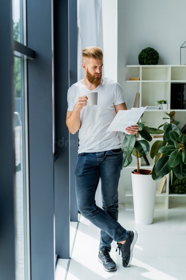 Bearded young businessman working at modern office.Man wearing white t-shirt and making notes on the documents.