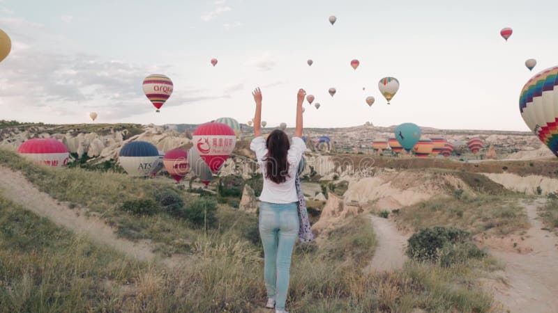 Young woman sunrise staying on the mountain with hot air ballons around. Steady cam shot