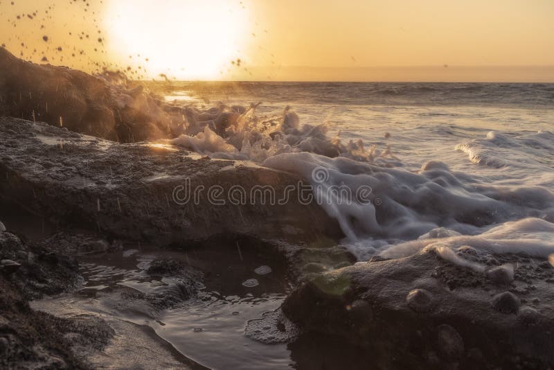 Beau coucher du soleil sur la plage sauvage du désert de Namibe avec le plan rapproché de l'eau de mer frappant les roches photos stock Beau coucher du soleil sur la plage sauvage du désert de Namibe avec le plan rapproché de l'eau de mer frappant les roches photos stock