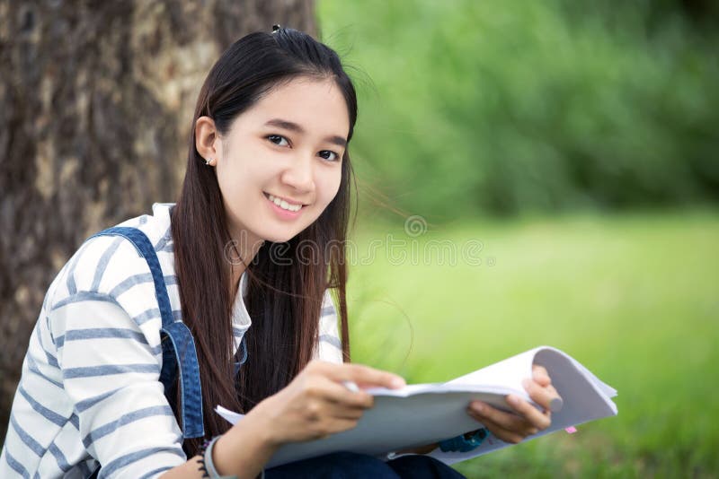 Beau livre et fonctionnement de lecture asiatique de sourire de fille à l'arbre dessus photographie stock Beau livre et fonctionnement de lecture asiatique de sourire de fille à l'arbre dessus photographie stock