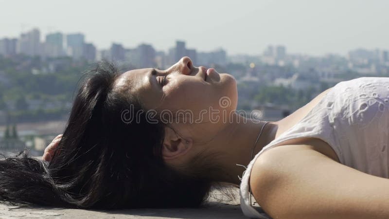 Beau mensonge de femme du bord du dessus de toit appréciant le soleil, ligne de ciel de ville sur le fond