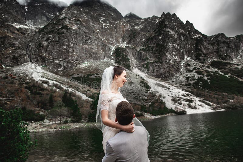 Beau photosession l'?pousant Le mari? entoure sa jeune jeune mari?e, sur le rivage du lac Morskie Oko poland photographie stock Beau photosession l'?pousant Le mari? entoure sa jeune jeune mari?e, sur le rivage du lac Morskie Oko poland photographie stock