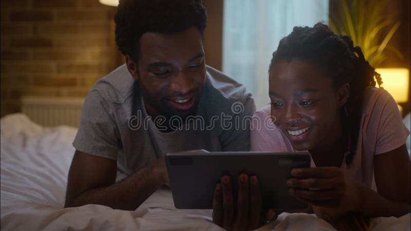 Un charmant couple afro-américain marié, une femme et un homme, riant et allongés sur le lit en utilisant une tablette numérique p clips vidéos