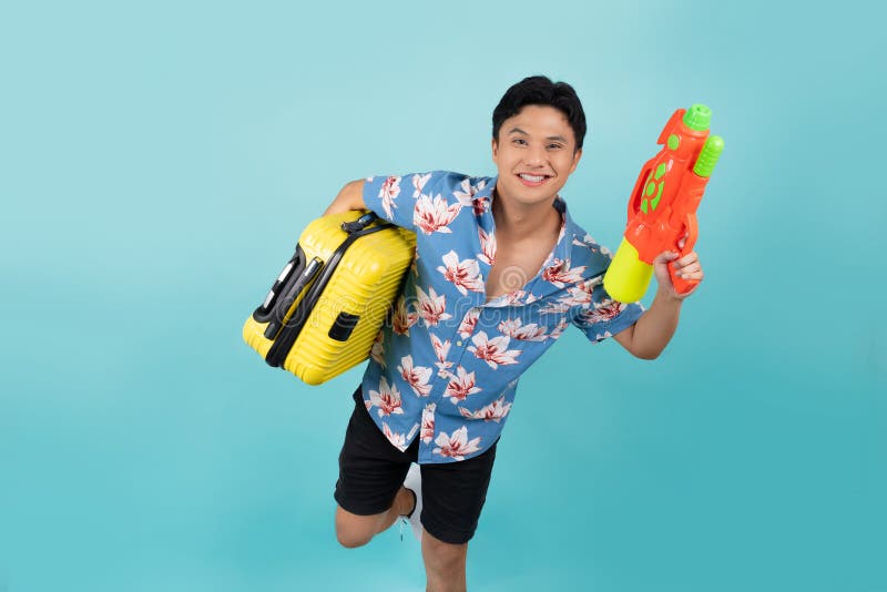Beau touriste asiatique en vêtements d'été avec pistolet à eau et bagages pendant le festival de songkran sur fond bleu image stock